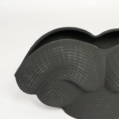 Detailed closeup of black ceramic sculpted vase showcasing curved layered design and matte textured surface.