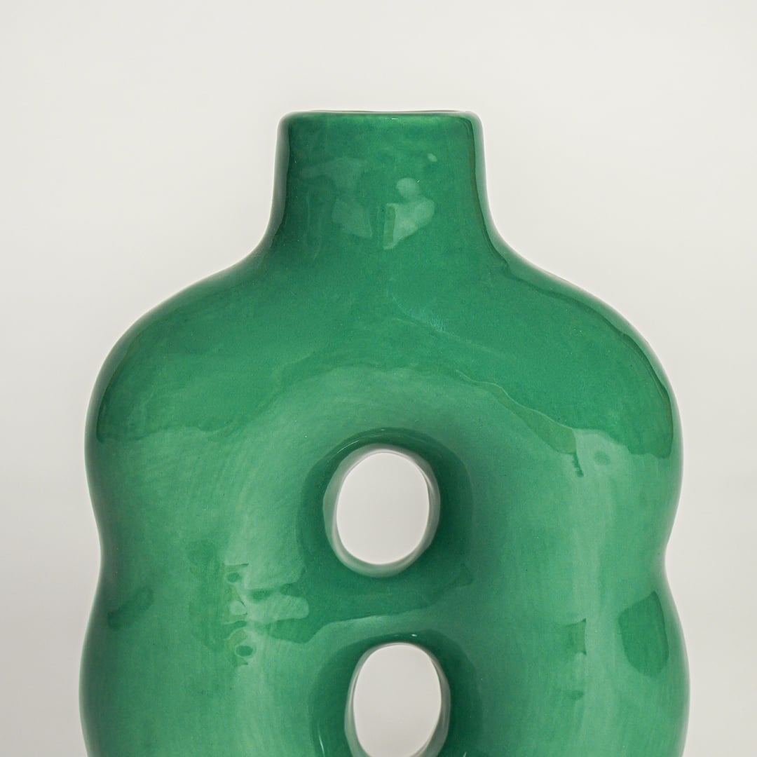 Closeup of green glazed ceramic vase showing smooth finish curved body and unique dual hole design.