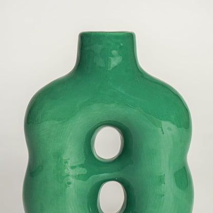 Closeup of green glazed ceramic vase showing smooth finish curved body and unique dual hole design.