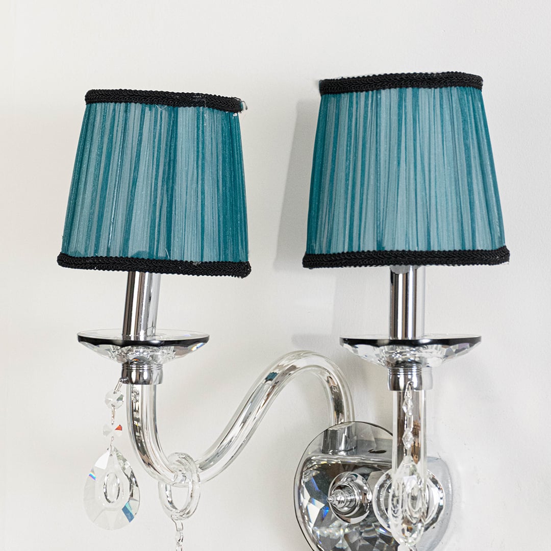 Closeup of double arm wall light with chrome base blue fabric shades and crystal drops for home decoration.