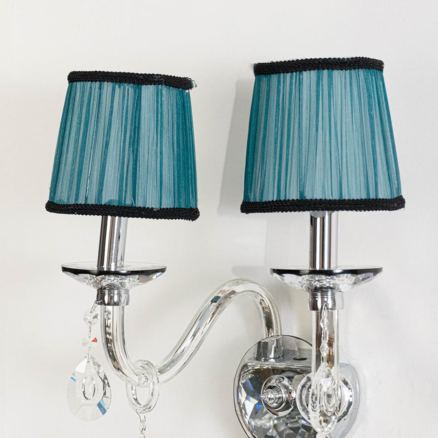 Closeup of double arm wall light with chrome base blue fabric shades and crystal drops for home decoration.