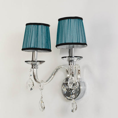 Double arm wall light with chrome base and blue fabric shades turned off with crystal drops on white background.