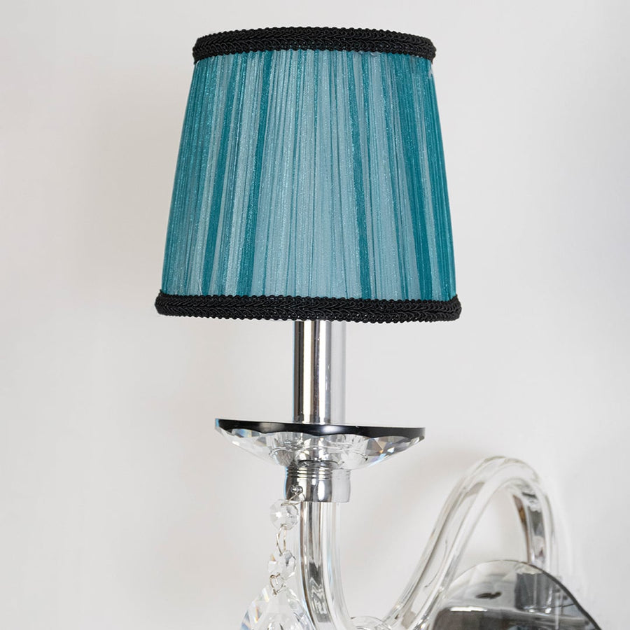 Closeup of wall light with chrome base blue fabric shade and crystal drops for elegant home decoration.