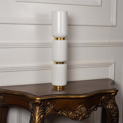 Glossy white tiered ceramic totem vase with gold structural rings displayed on a classic wooden console table for decor.