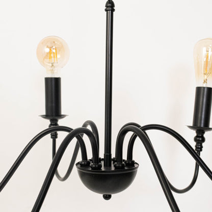 Detailed closeup of amber Edison globe bulb with black metal candle holder socket on vintage style chandelier curved arms.