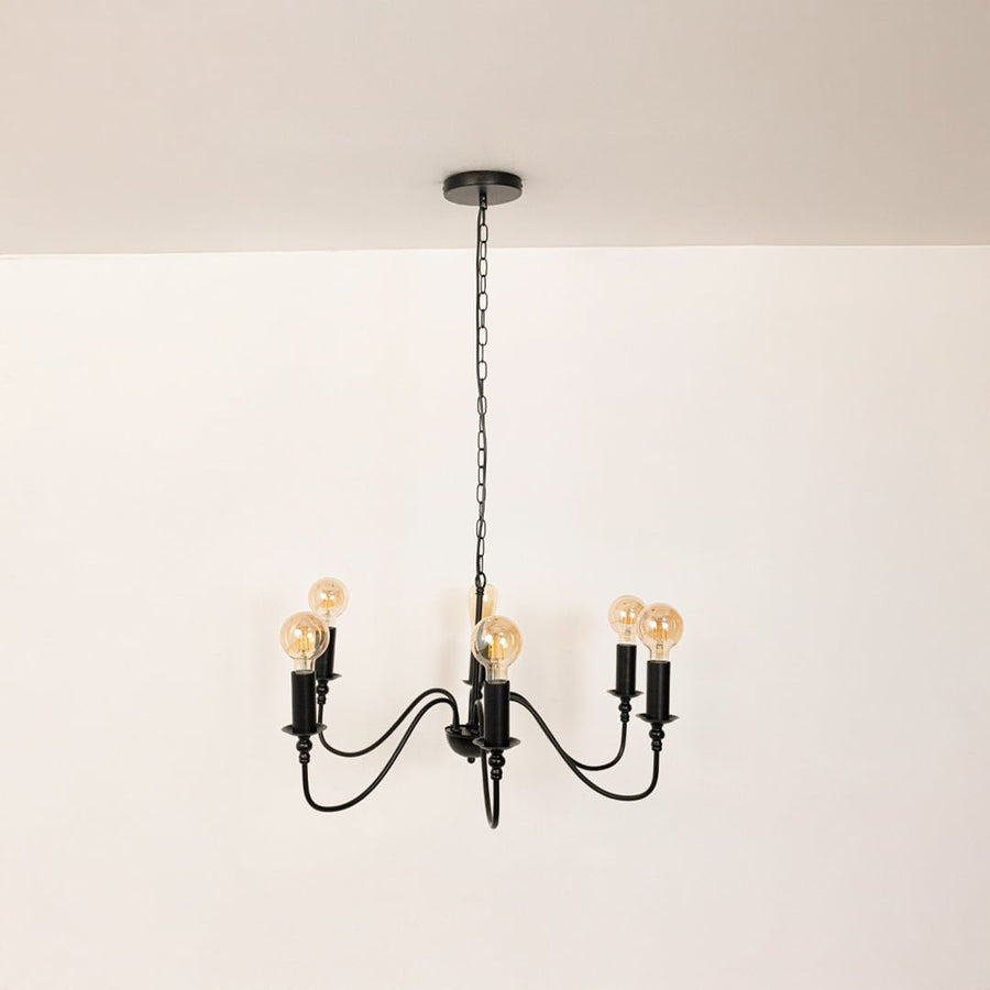 Detailed closeup of amber Edison globe bulb with black metal candle holder socket on vintage style chandelier curved arms.