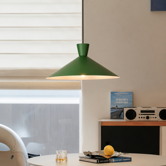 A green metal pendant light hangs over a dining table in a modern room setting with a window, radio, and books visible in the background.