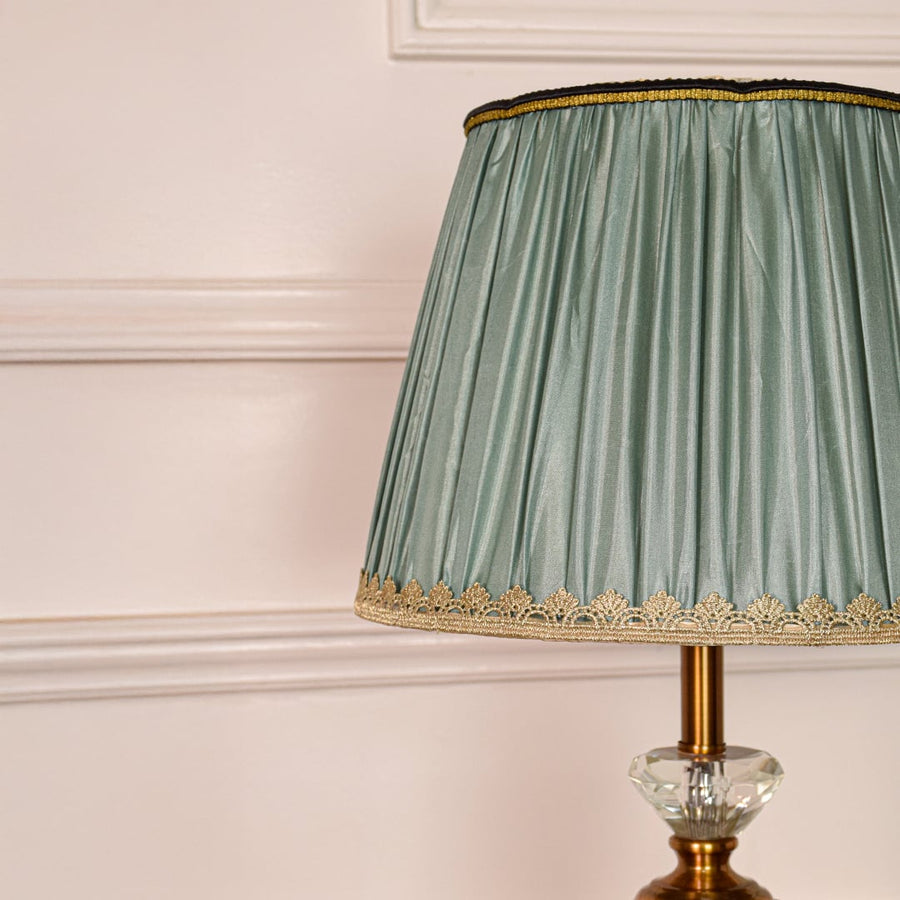 Closeup of table lamp highlighting clear glass stem faceted crystal detail gold metal finish and pleated teal shade.