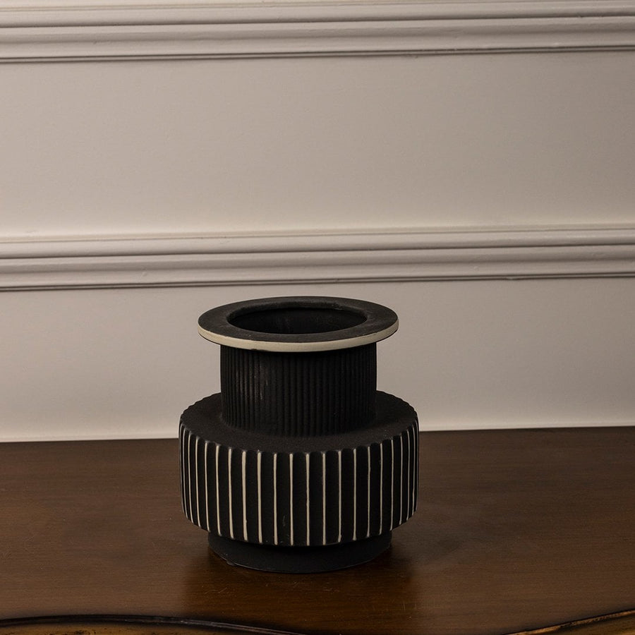 Elegant ribbed ceramic vase in black with white rim and base placed on white background for contemporary home decoration.