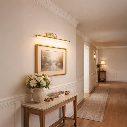 Gold metal picture light accentuating framed artwork above console table with refined gallery inspired decorative lighting.