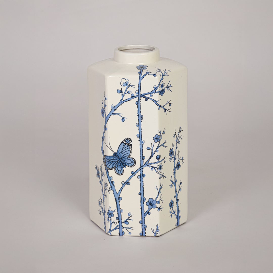 Decorative cream ceramic vase with blue flower pattern placed on white background emphasizing artistic printed surface.