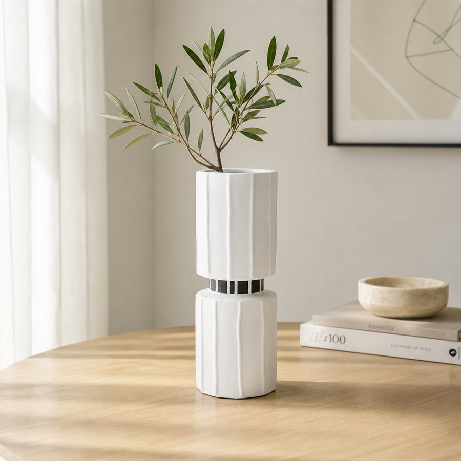 White ceramic flower vase with green stems placed on wooden table for elegant modern home decor styling.