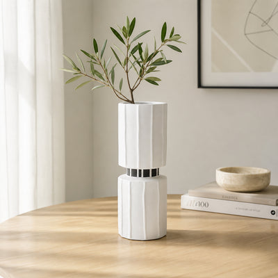 White ceramic flower vase with green stems placed on wooden table for elegant modern home decor styling.
