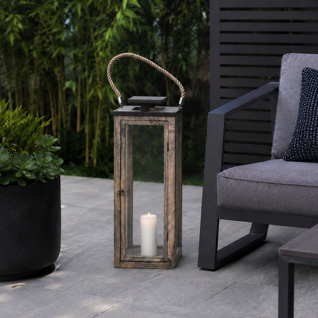 Wooden lantern with a candle on a patio next to a gray cushioned chair.