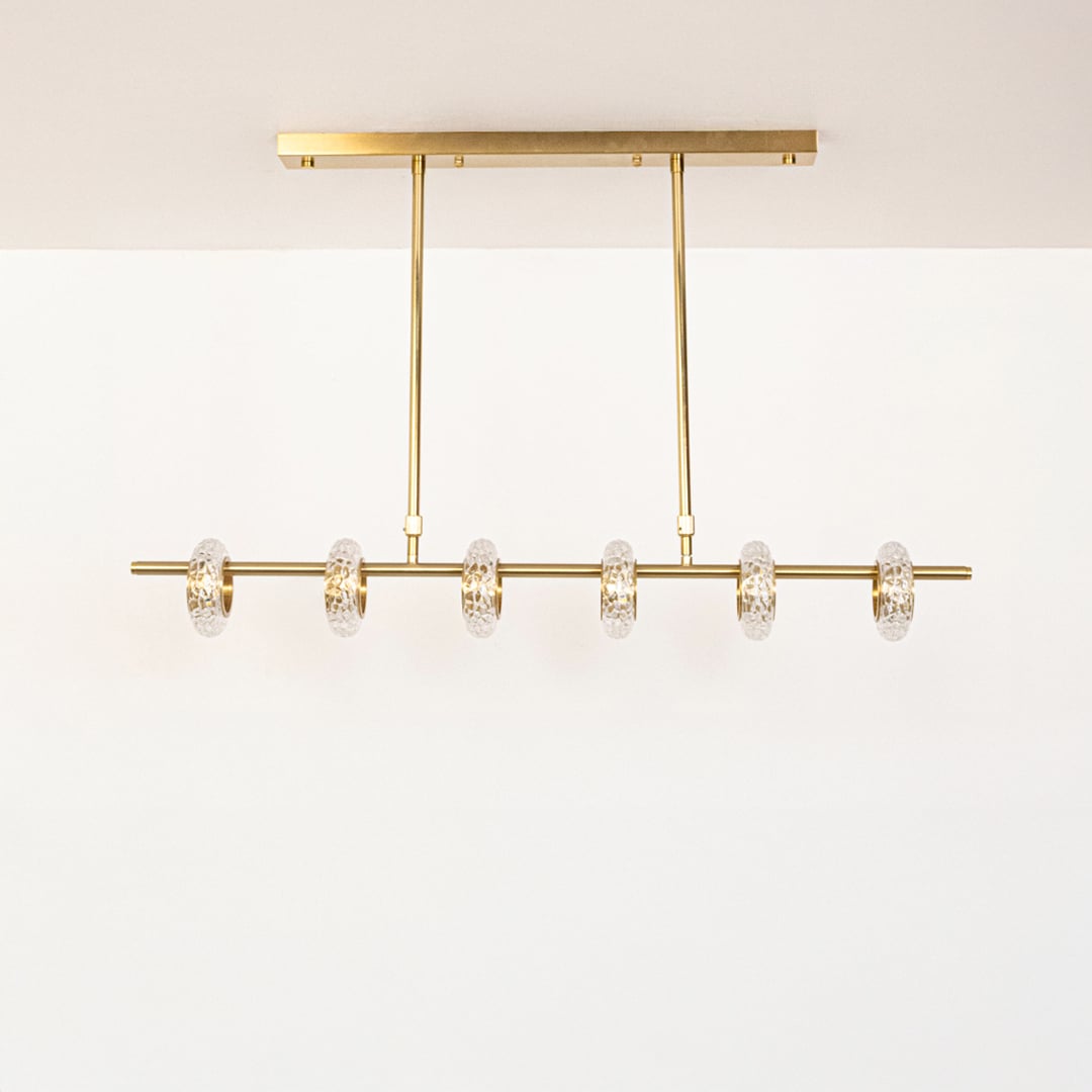 Golden metal linear chandelier with clear glass rings displayed off on white background highlighting elegant home lighting.