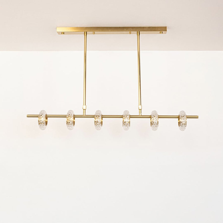 Golden metal linear chandelier with clear glass rings displayed off on white background highlighting elegant home lighting.
