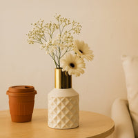 Ivory geometric ceramic vase with gold neck styled with white daisies and baby’s breath on a light wooden table for modern minimal decor.