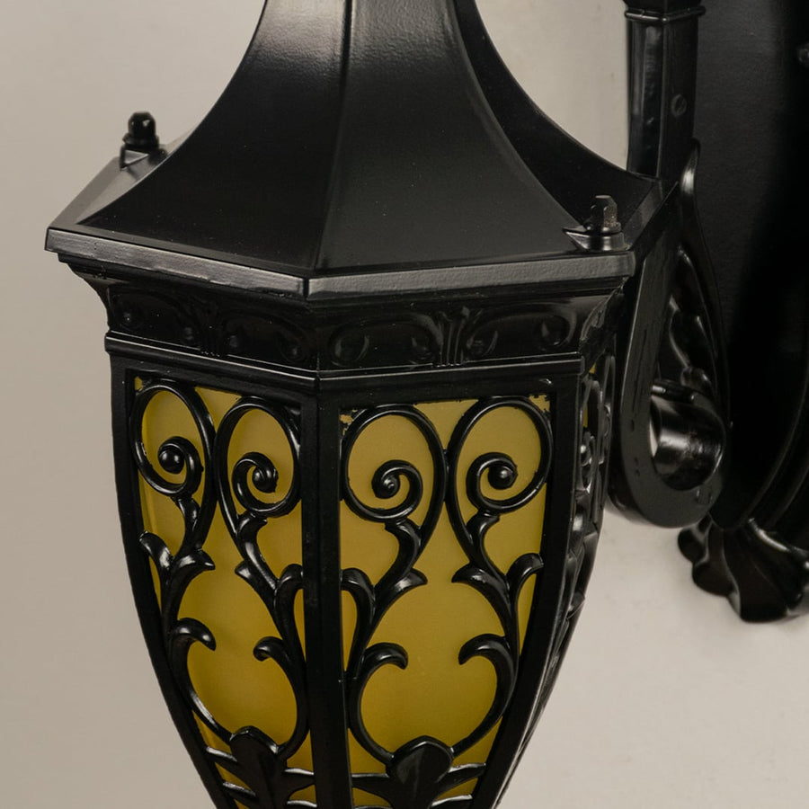 Detailed closeup of an ornate black outdoor lantern showcasing intricate metalwork and amber glass.