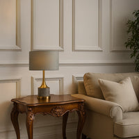 White shade gold table lamp on wooden side table with light off beside grey sofa for clean modern décor.
