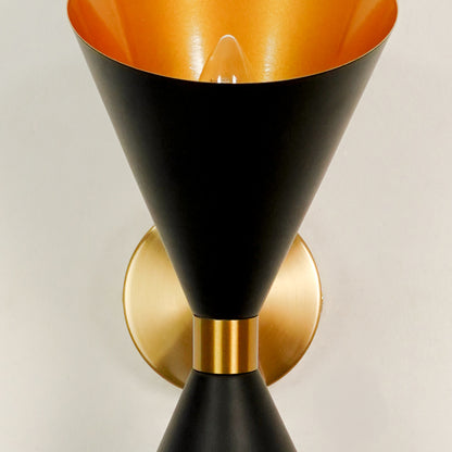 Close up details of an illuminated black and gold brass hourglass wall sconce showcasing the internal golden cone lining.