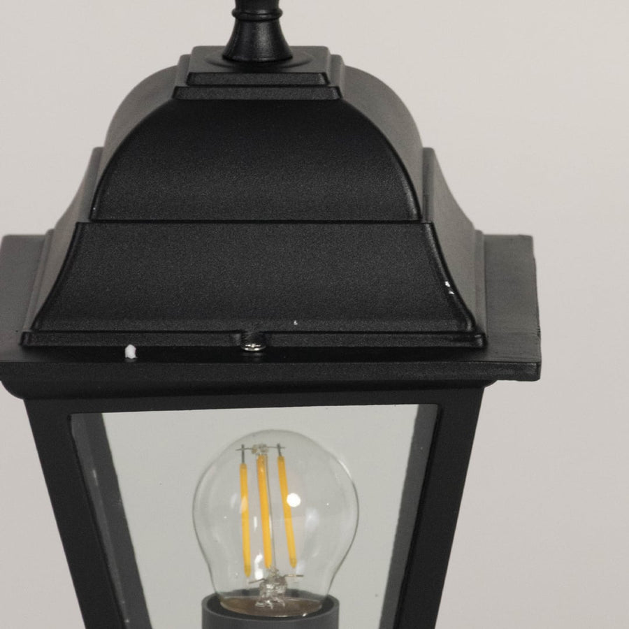 Closeup of black pillar lamp with glass shade and bulb showcasing elegant design for outdoor home garden and gate lighting.