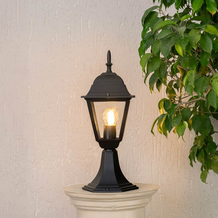 Stylish black pillar lamp glowing on stone pillar creating warm ambiance for outdoor home entrance and garden pathway.