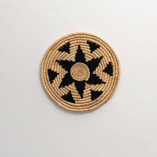 Round handcrafted natural seagrass wall basket with black star pattern on white background image.