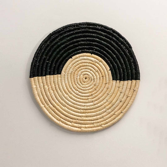 Round handcrafted black and cream woven seagrass wall basket with minimalist color block half design on white background.