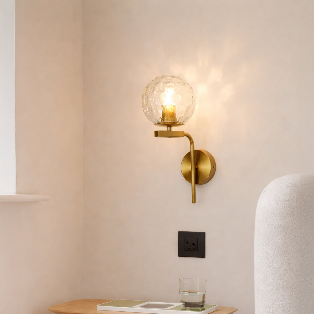 Modern gold metal wall light with textured glass globe for elegant bedroom and luxury decor styling spaces.