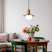 White globe pendant light with gold fixture installed above dining table in modern interior setting creating warm ambient lighting decor styling.