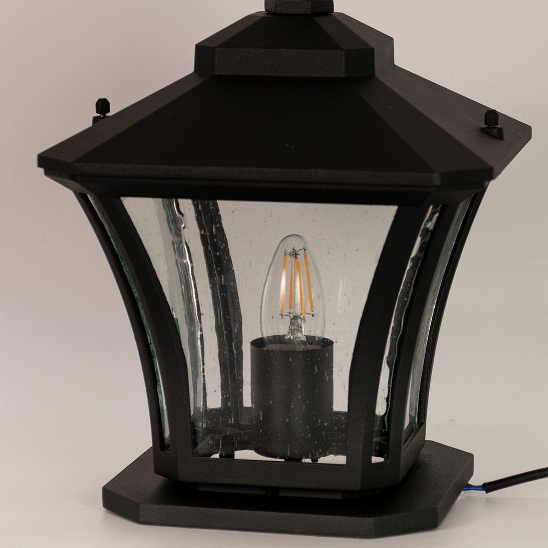 Closeup view of black metal pillar lantern highlighting clear ribbed glass panels and premium outdoor build quality.
