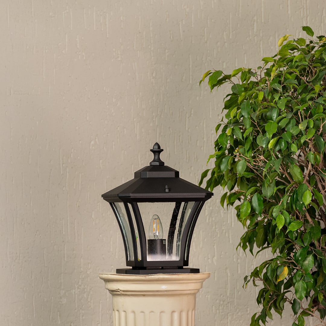 Black pillar lantern crafted in metal with clear textured glass shown unlit for outdoor home entrance styling.