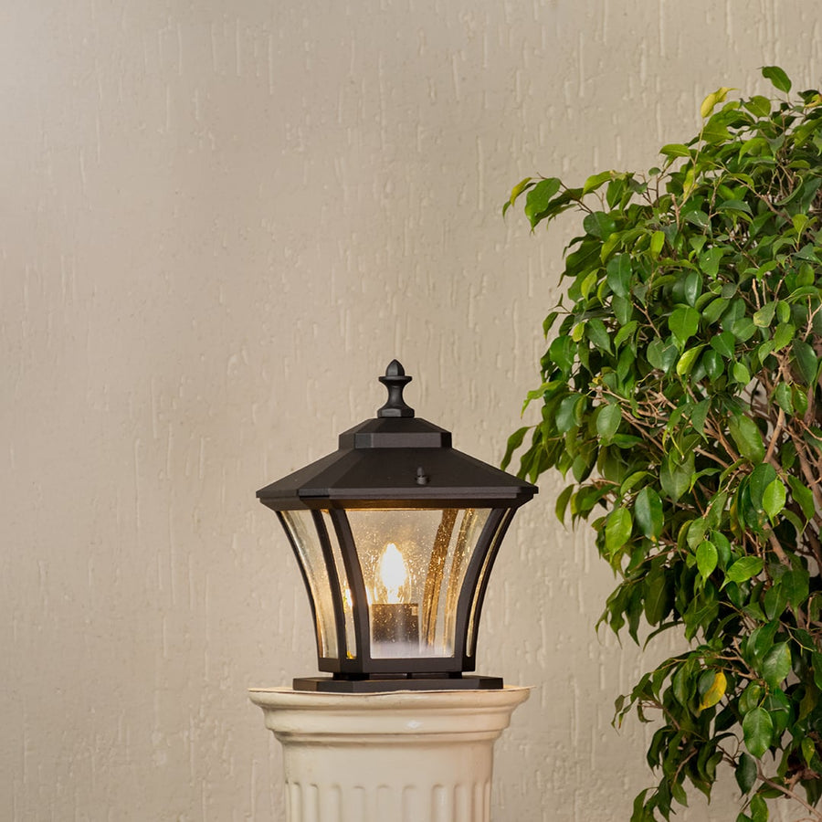 Elegant black metal pillar lantern glowing warmly with clear glass panels for outdoor garden or porch lighting.