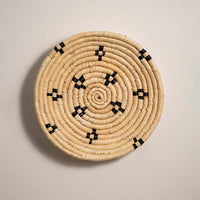 Medium round woven wall basket featuring natural beige grass with black stitched patterns isolated on a white background for wall decor.