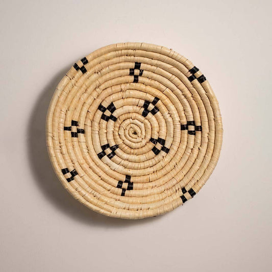 Round handcrafted natural cream seagrass wall basket with small black geometric diamond accents on white background image.