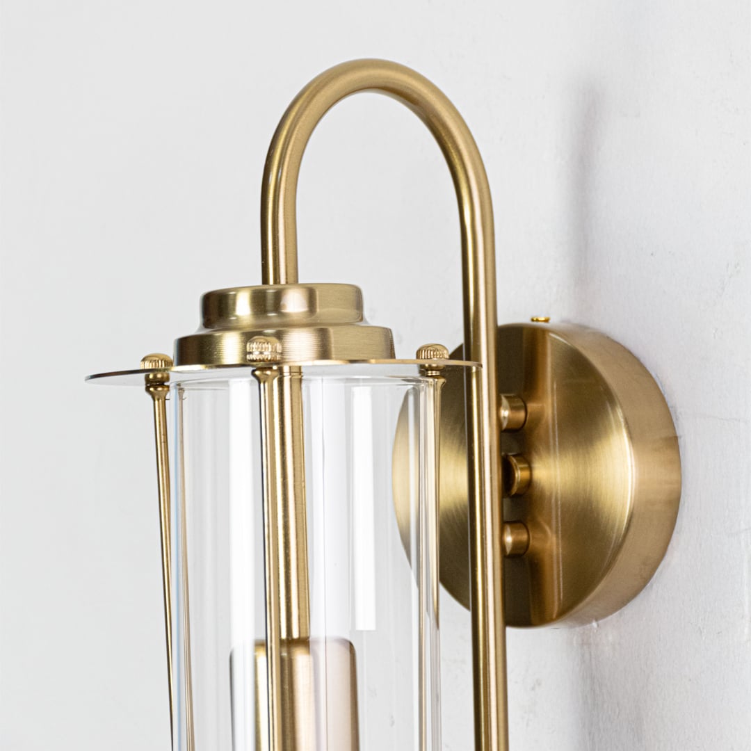 A detailed closeup of the gold wall sconce showing the smooth metal finish and clear glass shade highlighting the refined craftsmanship.