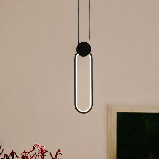 A modern pendant light with a vertical oval frame, featuring a glowing white LED light inside and a matte black top cap, hanging against a warm beige wall.