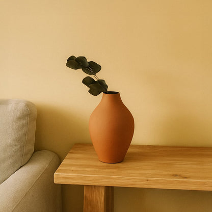 A warm toned room scene featuring a terracotta vase with a single eucalyptus stem placed on a wooden side table beside a soft beige sofa adding calm modern decor charm.