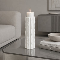 White textured candle holder with white candle placed on glass table for elegant home decor styling.