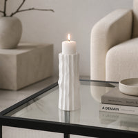 White textured candle holder with white candle placed on glass table for modern decor styling.