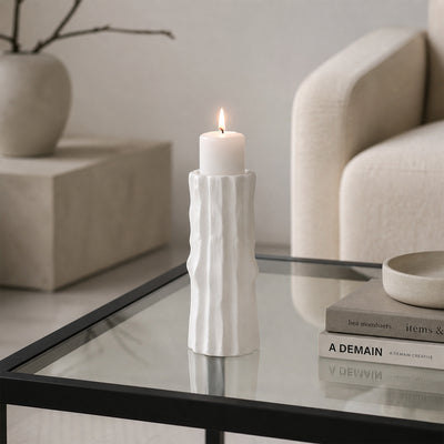 White textured candle holder with white candle placed on glass table for modern decor styling.