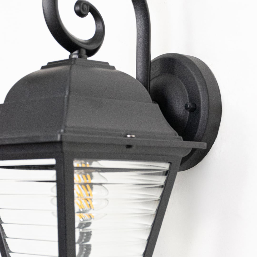 Closeup view of black metal wall lantern highlighting ribbed clear glass panels curved arm and sturdy construction.