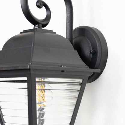 Closeup view of black metal wall lantern highlighting ribbed clear glass panels curved arm and sturdy construction.