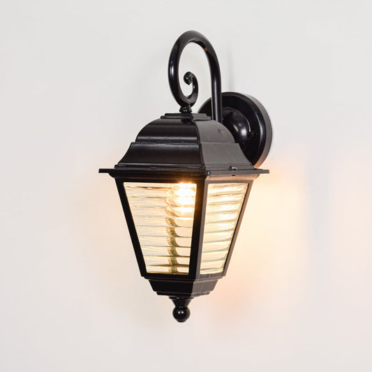 Black metal outdoor wall lantern switched on displayed on white background producing warm welcoming exterior illumination.