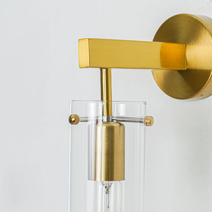 Close up gold metal wall light with sleek cylindrical glass design mounted on neutral wall background for elegant decorative lighting setup.