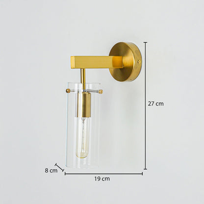 Modern gold wall light with clear glass cylinder shade mounted on neutral wall background 27 cm height 19 cm width 8 cm depth ideal for bedroom or hallway lighting.