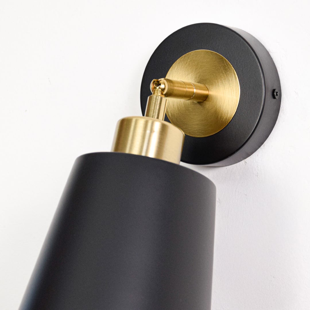 Black metal wall light closeup featuring brushed gold holder and wall mount detail emphasizing premium modern lighting craftsmanship.