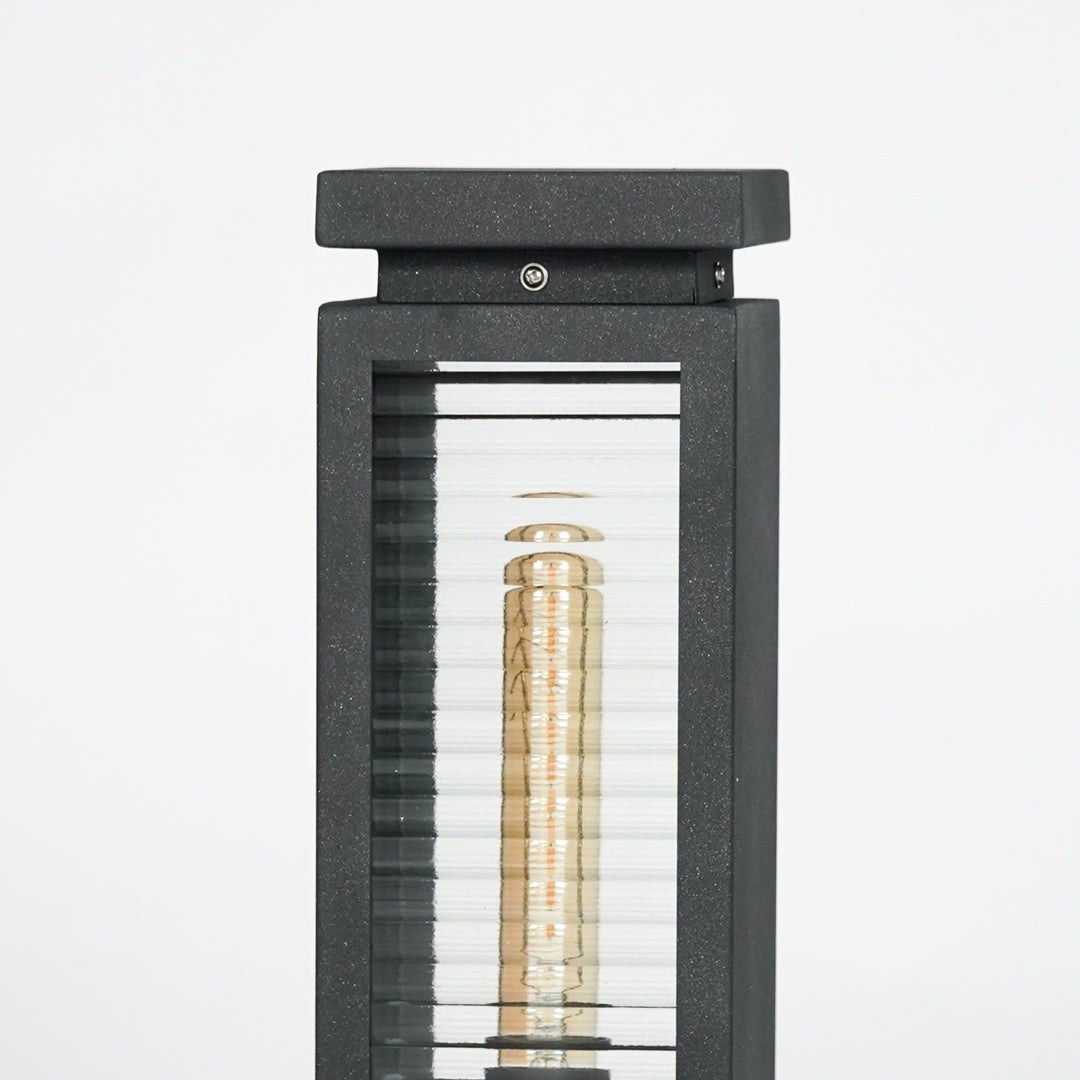 Closeup of black metal outdoor bollard light with clear glass panels for elegant exterior lighting decor styling.