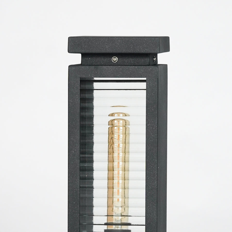 Closeup of black metal outdoor bollard light with clear glass panels for elegant exterior lighting decor styling.