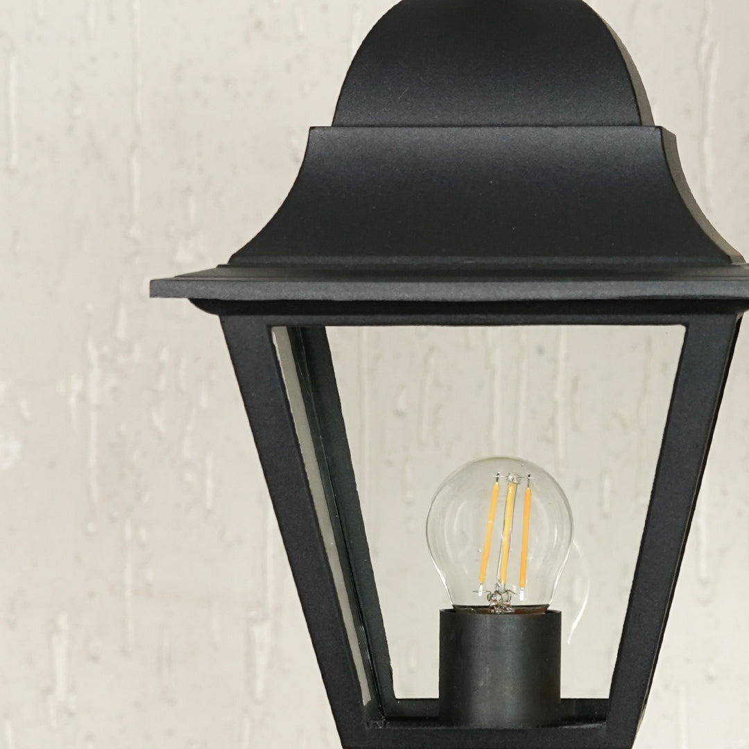 Closeup of black outdoor gate light with clear glass shade and metal frame for modern decor styling.